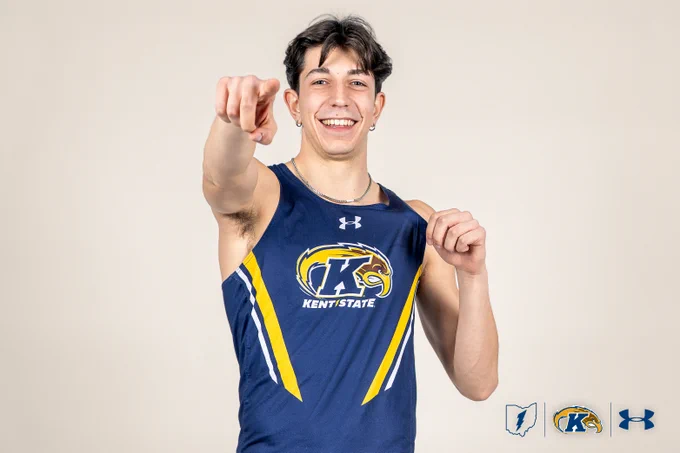A person in a Kent State athletic uniform stands smiling, pointing towards the camera. The uniform displays the Kent State logo. The logos of Under Armour and Kent State are visible in the lower right corner.