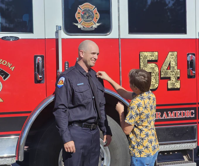 Captain Croft stands in front of CAFMA Engine 54 as one of his sons pins his badge on his uniform.