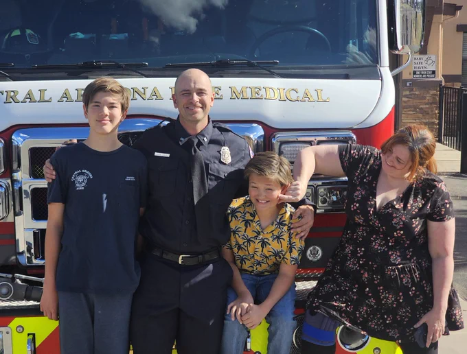 Captain Croft, his wife, and two sons smile together in front of a fire engine.
