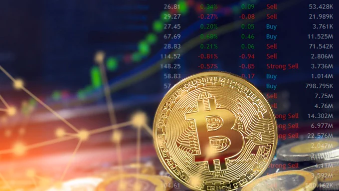 Close-up of a golden Bitcoin coin with a blurred digital stock market chart and trading data in the background.