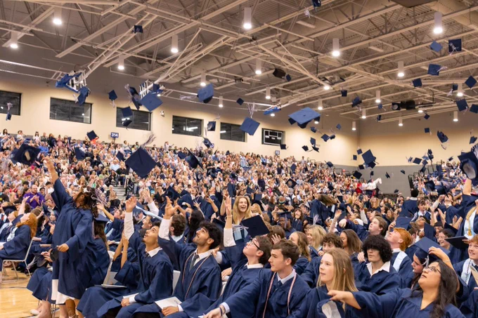 Graduation ceremony with a large crowd of students in blue gowns and mortarboards seated in rows.