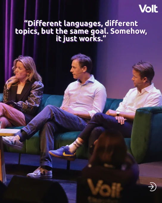 Three people sit on a green velvet sofa during a panel discussion on a stage. They are dressed in business-casual attire and wearing headset microphones. Overlaid text reads: "Different languages, different topics, but the same goal. Somehow, it just works." The Volt logo is in the top right corner.