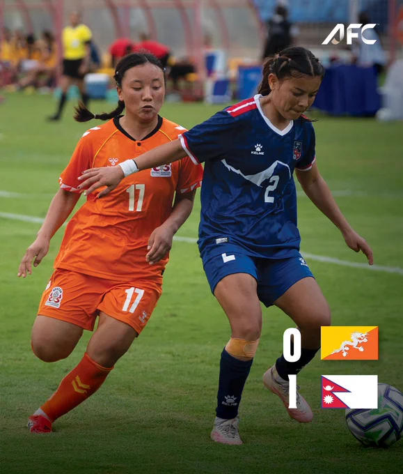 An intense moment during an AFC women's football game with players from Bhutan and Nepal competing for possession. The score shows Bhutan 0, Nepal 1. The mood is competitive and dynamic.