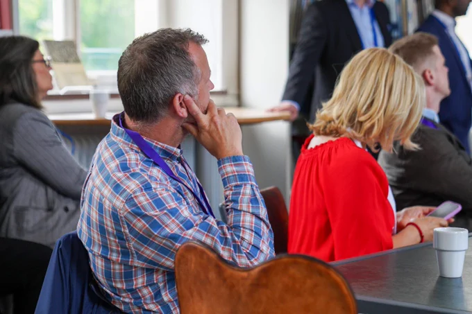 Man in plaid shirt attentively listening during a meeting in a bright conference room.