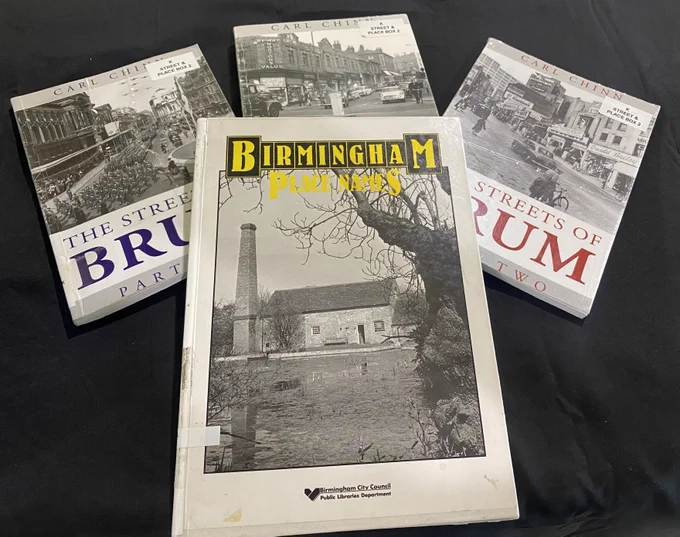 Four books laid on a flat surface  - three in the background and one in the foreground. The three books in the background are titled The Streets of Brum by Carl Chinn. Each has a section of a historic photograph of Birmingham on its front cover. The book in the foreground is titled Birmingham Place Names and has a photograph of a mill by a pool on its front cover.