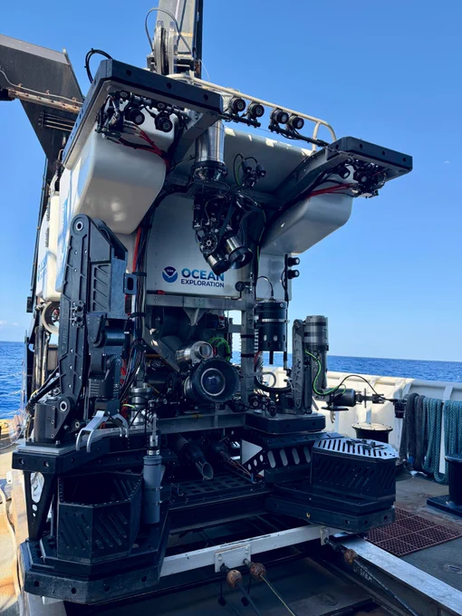 ROV Deep Discoverer sits on a ship's open deck at sea, showcasing a manipulator arm, sampling equipment, and camera systems.


