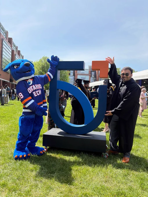 A photo of a graduating student posing with the Ontario Tech logo and Hunter in Polonsky Commons.
