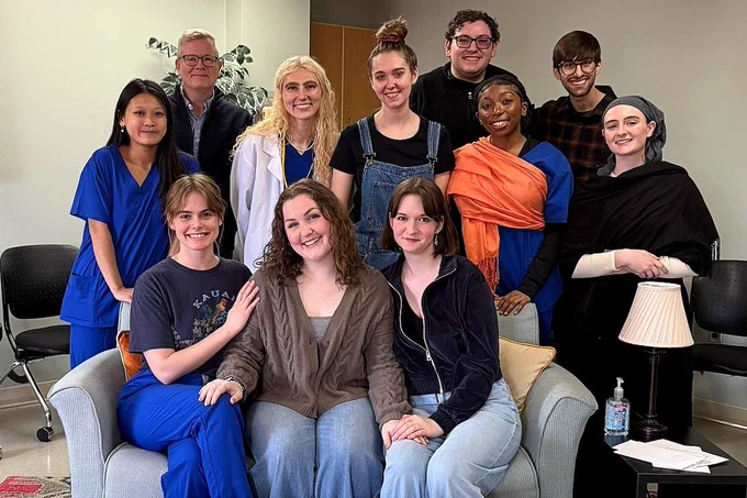 A group of ten diverse individuals, smiling and casually dressed, gather around a couch in a room. Their expressions convey warmth and camaraderie.