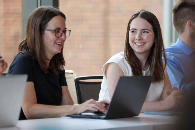 Two people sitting at a table, smiling, with a laptop open