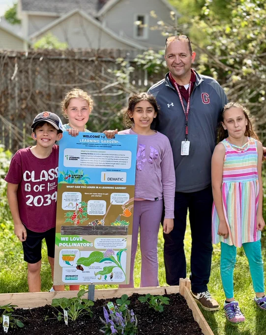 Principal stands by garden with four students outside on a sunny day