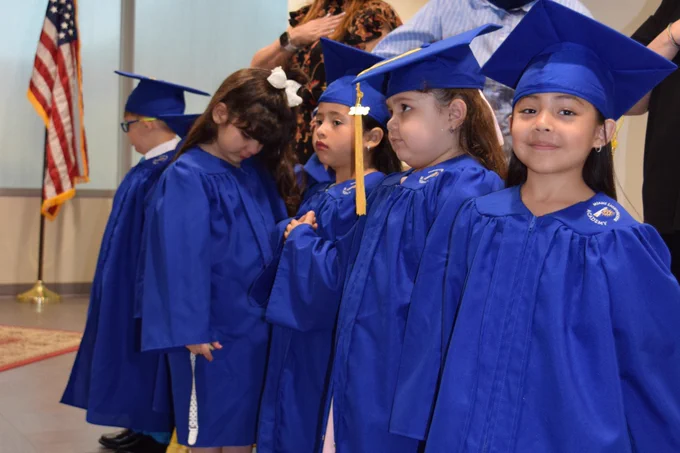 A candid photo of 5 children at their Pre-K graduation, with one child smiling at the camera.