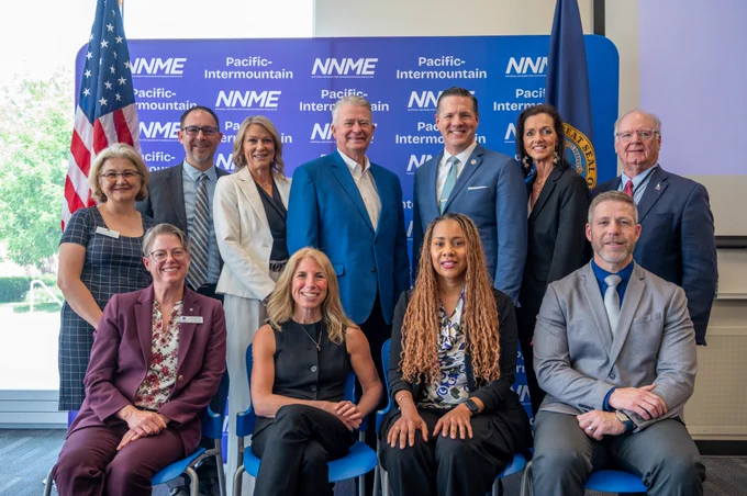 Eleven industry partners, officials and Boise State leadership pose for a formal group photo in front of a National Network for Microelectronics Education (NNME) blue backdrop for the Pacific Intermountain Network for Education in Semiconductors (PINES) regional node announcement event. 