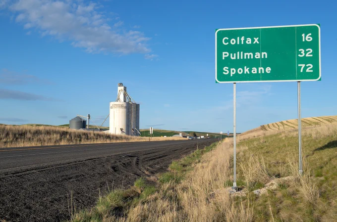Blue sky and white clouds are above a green sign with mileage to Pullman on the way to Washington State University Pullman, Friday, April 30, 2021. Distances are Colfax 16, Pullman 32, Spokane 72. 
