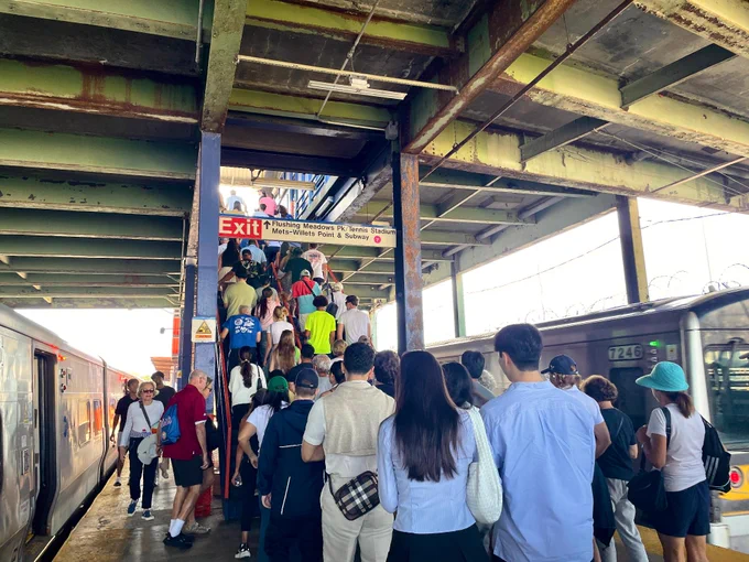 People walking up the stairs at Mets-Willets Point station platform during the daytime.