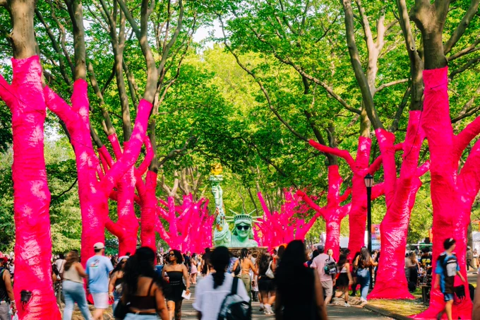 A crowd of people attending Gov Ball in a park with trees, with a green Statue of Liberty replica in the background.