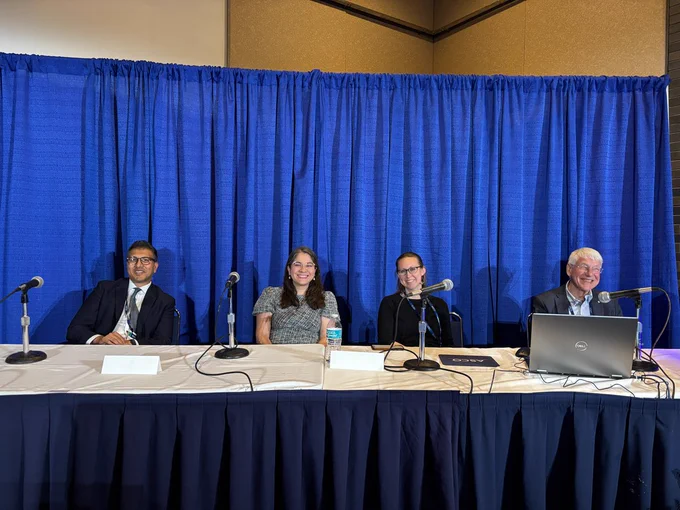 Panelists sitting at a long table against a blue curtain background.