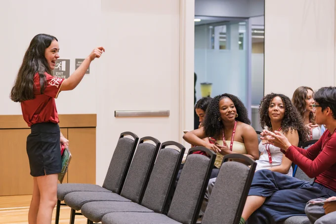 An orientation leader is laughing and talking with seated group of students.
