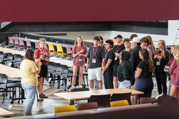 A orientation leader speaks to their group of new students. They are all casually dressed and wearing name tags.