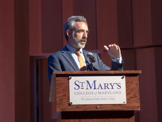 A man speaks at a podium. A sign that reads, "St. Mary's College of Maryland hangs on the podium."