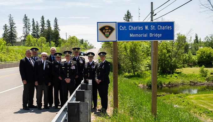 Gathering of individuals next to OPP Cst. Charles W. St. Charles Memorial Bridge sign