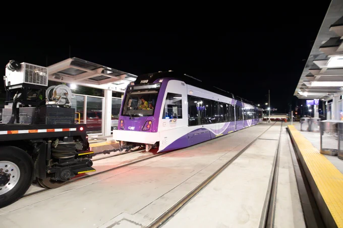 Modern purple and white light rail train stationed at a well-lit platform during nighttime.