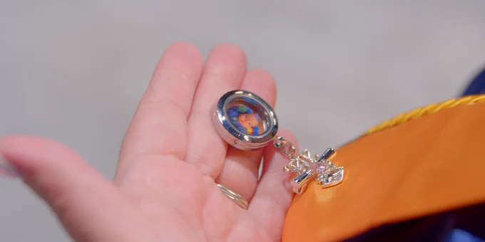 A hand is holding a locket with a small image inside.
