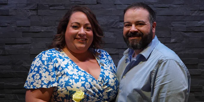 A man and a woman posing for a photo holding a rose.