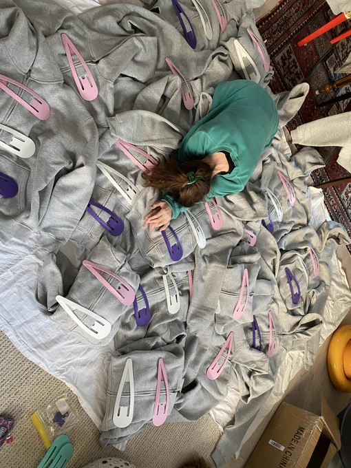 A person lies face down surrounded by large hair clips.