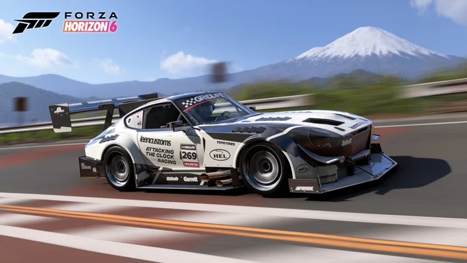 Race car from "Forza Horizon 6" on a track, set against a mountainous backdrop with a partially snow-covered peak. The car is white with sponsor decals, including visible logos and the number 269.