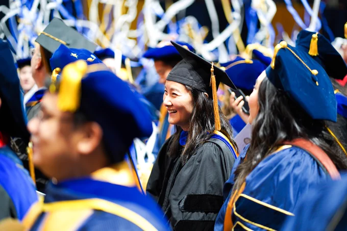 Faculty during Doctoral Ceremony smiling with students as confetti rains down.