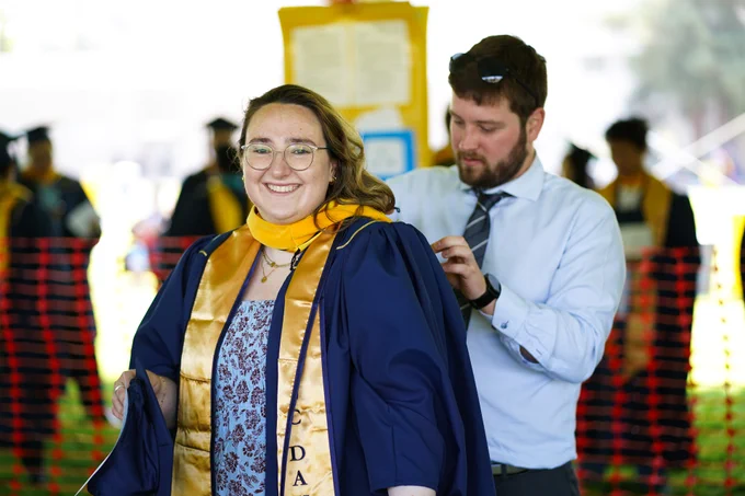 Masters student smiling as hood is adjusted.