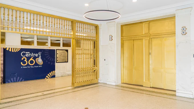 Interior view of the Centre 360 entrance area inside the David N. Dinkins Municipal Building, featuring gold elevator doors, marble walls, and Centre 360 signage.