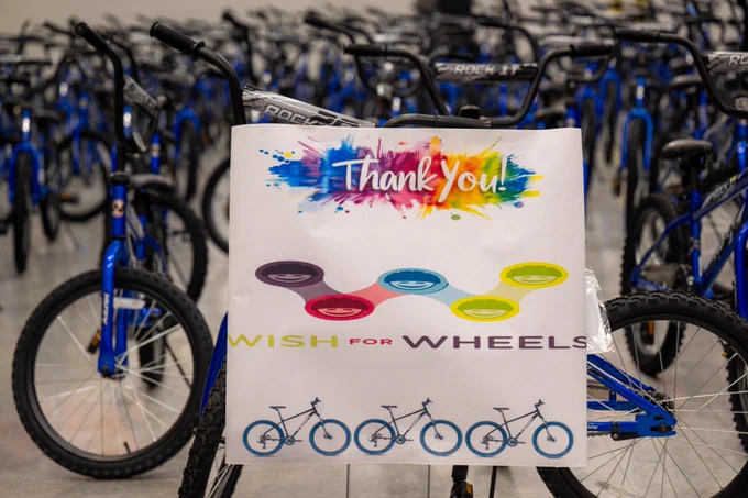 Hundreds of bikes sit on a gym floor, and a sign reads, "Thank you! Wish for Wheels."