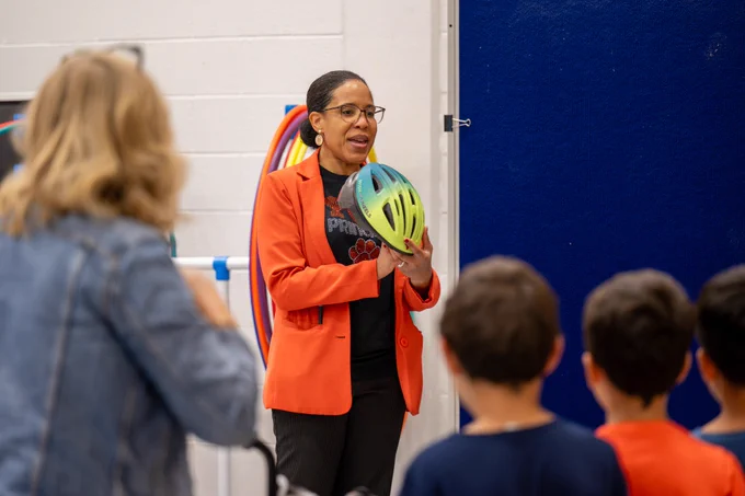 An adult holds up a helmet and shows it to students.