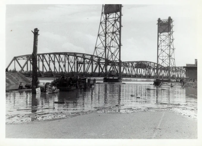 Historic black-and-white photo of the original span of the Interstate Bridge spanning the Columbia River, with two tall steel towers supporting the structure.