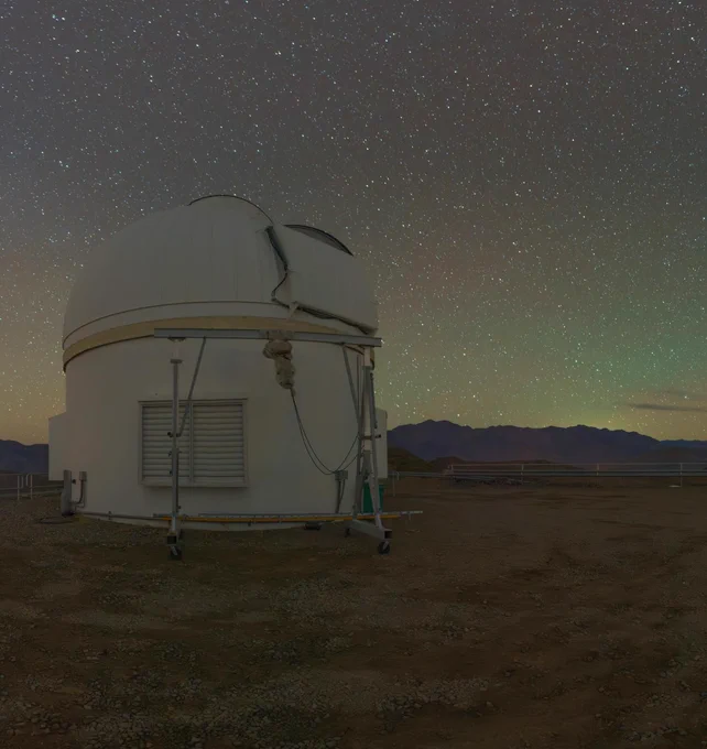 Panel four of four of a panoramic view from Cerro Pachón's rocky summit:  traditional cylindrical telescope building under a starry night sky.