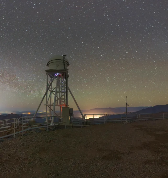 Panel three of four of a panoramic view from Cerro Pachón's rocky summit: a tall spindly tower topped with a small dome under a starry night sky.