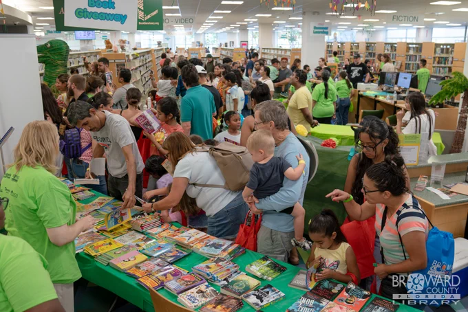 A large group of people in a library picking up free books from a table display