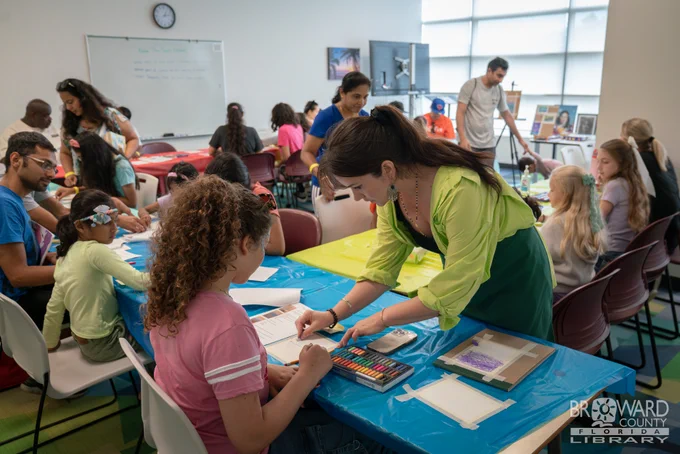 An illustrator helping a child with their artwork during a crowded drawing seminar