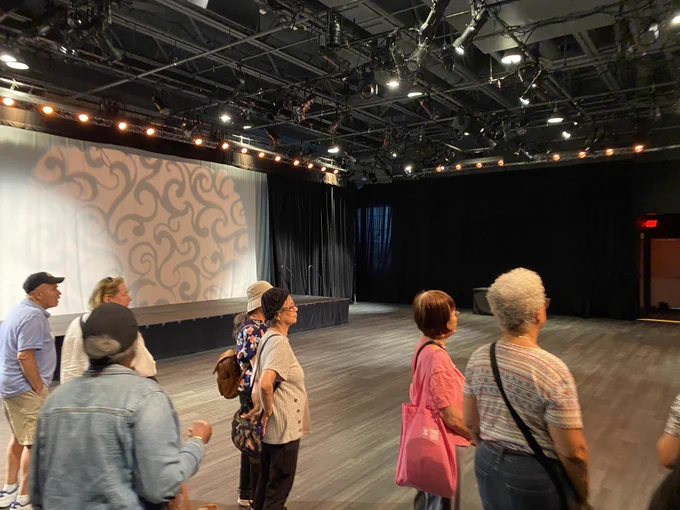 Group of people attentively watching a presentation in a spacious, dimly lit event hall with patterned wall projection.