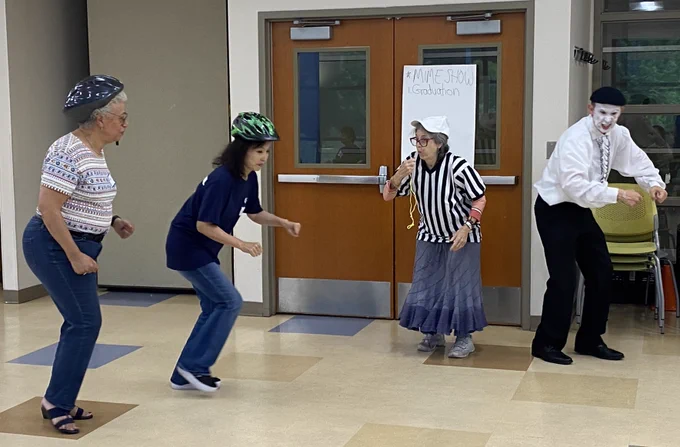 Four adults in a room engaged in an active game, two wearing helmets, one dressed as a referee holding a whistle, and another preparing to catch.