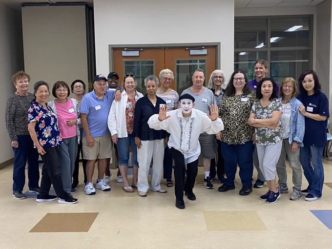 Group of diverse adults posing together in a community center hallway, smiling and standing casually in front of double doors.
