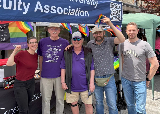 Five people pose together under a WLUFA tent decorated with Pride flags at the Pride and Popsicles event.