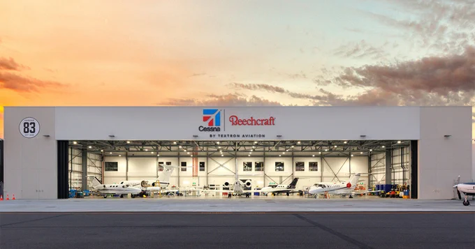 Modern aircraft hangar at sunset featuring Cessna and Beechcraft logos, displaying several small business aircraft inside.