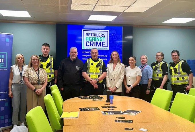 Group of police officers and civilians posing in front of a "Retailers Against Crime" screen.