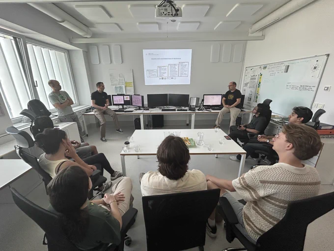 Water-R20 NRT students listen to a presentation on hydrologic forecasting in a university research facility in Slovenia, with computers and monitoring systems visible.