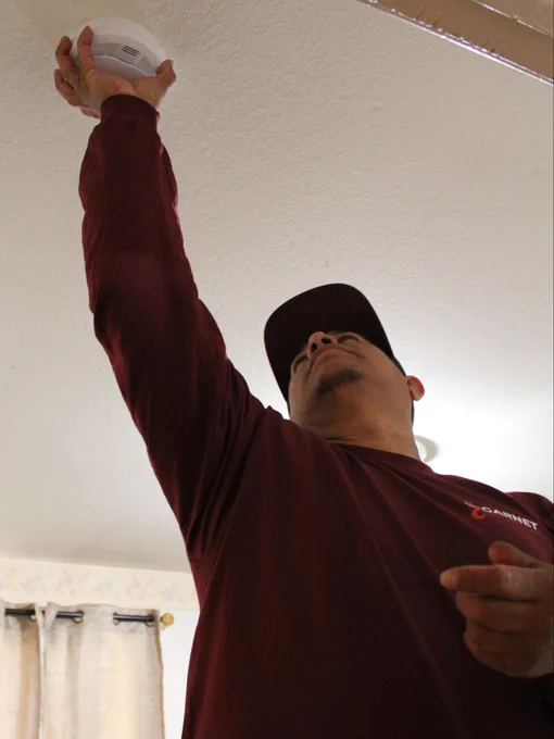 A volunteer installs a smoke alarm on the ceiling of a room