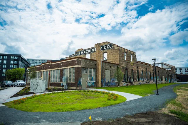 The Malcolm Yards Food Hall building surrounded by a green lawn and modern buildings in the background. Blue sky with scattered clouds.