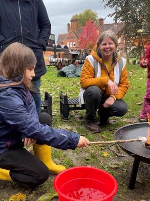 Children and adults toasting marshmallows over a fire pit outdoors on an autumn day.