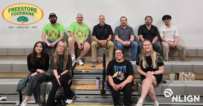 A group of 10 NLign employees both men and women sitting on the steps of the Freestore Foodbank in Cincinnati, smiling for the camera.